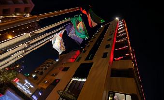 a tall building with colorful flags hanging from the lights , illuminating it at night in a dark environment at Swiss-Belboutique Bneid Al Gar Kuwait