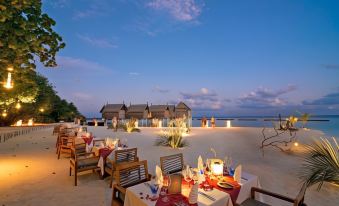 a beach resort with a dining area set up on the sand , surrounded by palm trees at Constance Moofushi