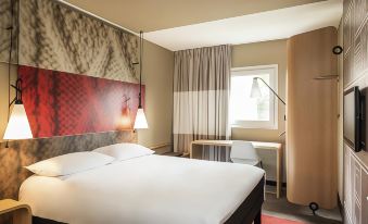 a hotel room with a red and white striped headboard , two lamps on either side of the bed , and a desk in the corner at Ibis Mulhouse Bale Aeroport