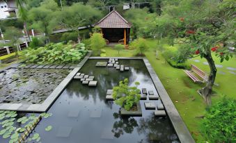 a beautiful garden with a pond , surrounded by lush greenery and a gazebo , creating a serene atmosphere at Hotel Cianjur Cipanas