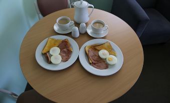 a table with two plates of breakfast food , including eggs and ham , next to cups of coffee at Ballina Colonial Motel