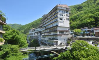 a tall building is situated next to a river with a bridge connecting it to the other side at Zazan Minakami