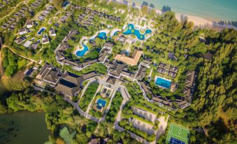 a bird 's eye view of a resort with multiple buildings , pools , and grassy areas near the beach at Robinson Khao Lak