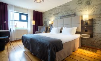a large bed with a blue blanket and white pillows is in a room with wooden floors at Clarion Collection Hotel Carlscrona