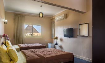 a hotel room with two beds , a window , and a tv , all set against a backdrop of the great pyramids of giza at Pyramids View Inn