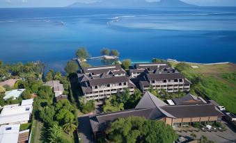 a large hotel is situated on the shore of a lake , with mountains in the background at Te Moana Tahiti Resort