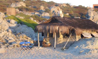 a beach house with a thatched roof , surrounded by sand and rocks , is set up on a hill at Villa del Faro