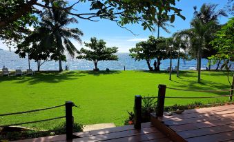 a grassy area near a body of water , with a wooden deck and palm trees in the foreground at Lomtalay Resort Trat