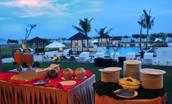 a table with a red cloth is set up in front of a pool , surrounded by stacks of plates and cups at The Jayakarta Suites Komodo Flores