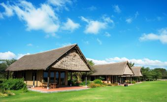a group of wooden houses with thatched roofs , situated on a lush green lawn under a blue sky at Sweetwaters Serena Camp