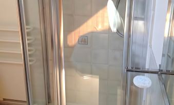 a shower stall with a white tiled wall and a glass door , next to a wall that has a towel hanging on the door at Chalk and Cheese