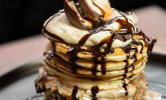 a tall stack of pancakes topped with ice cream , whipped cream , and chocolate sauce at Arthouse Hotel