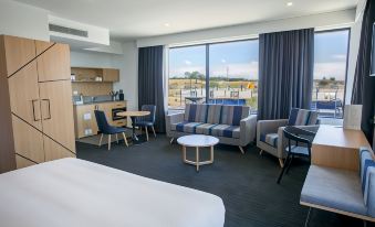 a modern hotel room with a bed , couch , dining table , and chairs , as well as a view of the ocean at Alpha Hotel Eastern Creek