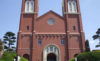 a large red brick church with two tall steeple towers , surrounded by a fence and trees at Nagasaki Nisshokan