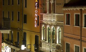 a city street at night , with a tall hotel building on one side and a pizza shop on the other at Hotel Nazionale