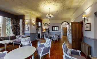a spacious living room with wooden floors and white furniture , including chairs and a dining table at Nunsmere Hall Hotel