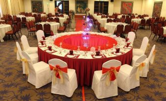 a large , round table is set with white and red linens , chairs , and a centerpiece in the center at Good Hope Hotel