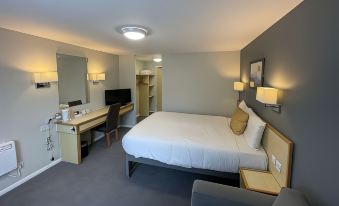 a large , neatly made bed is in the middle of a room with a desk and chair at Days Inn by Wyndham Sedgemoor M5