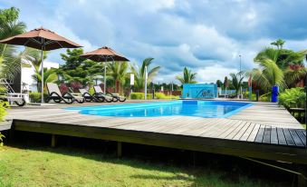 a large outdoor swimming pool surrounded by grass and trees , with lounge chairs and umbrellas placed around the pool area at Lakeview Terrace Resort Pengerang