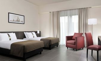 a modern hotel room with two beds , a window , and a red armchair near the window at Inn Naples Airport