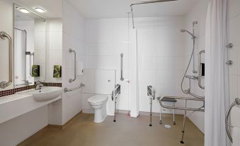 a modern bathroom with white walls , shower area , toilet , and grab bars , as well as a sink and toilet at Premier Inn Derby East