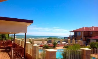 a balcony overlooking the ocean , with a swimming pool and a view of the beach at Seaspray Beach Holiday Park