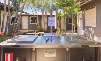 a stainless steel kitchen counter with a grill top and shelves , surrounded by a tropical environment at Econo Lodge Karratha