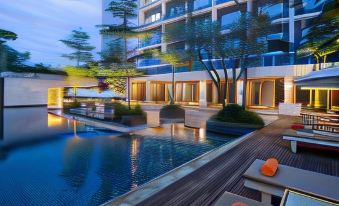a modern apartment building with a large swimming pool , surrounded by lush greenery and outdoor seating at Delonix Hotel Karawang