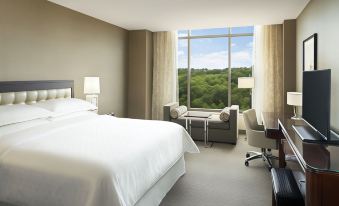 a hotel room with a large bed , a desk , a chair , and a window overlooking a forest at Sheraton Austin Georgetown Hotel & Conference Center