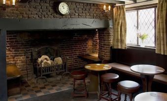 a cozy restaurant with brick walls , wooden tables , and stools , a fireplace , and a clock on the wall at The Brocket Arms