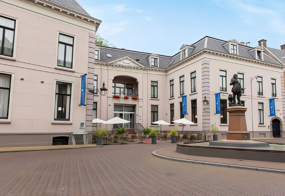 a large brick building with a fountain in front of it , surrounded by chairs and umbrellas at Fletcher Hotel Paleis Stadhouderlijk Hof