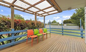 a wooden deck with three colorful chairs placed on it , overlooking a beautiful landscape of trees and grass at North South Holiday Park