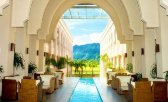 a modern indoor pool area with large windows , wooden benches , and tropical plants , overlooking a mountainous landscape at The Pade Hotel