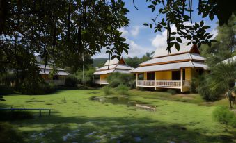 a row of yellow and white houses surrounded by a grassy field , with trees in the background at Poonyamantra Resort