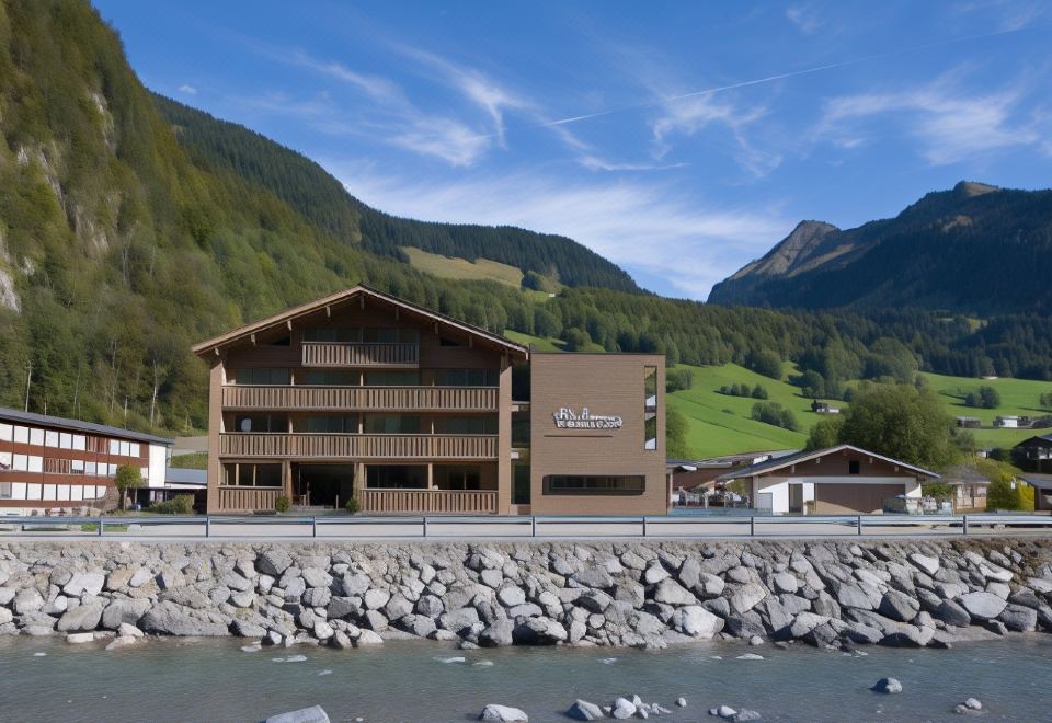 a large wooden building with a brown facade is situated next to a body of water at Hotel Hubertus - Au Bregenzerwald