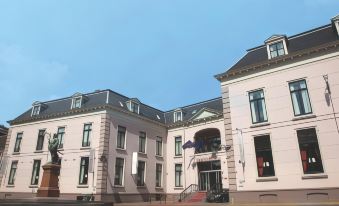 a grand pink building with a statue in front , under a clear blue sky , under a clear white sky at Fletcher Hotel Paleis Stadhouderlijk Hof