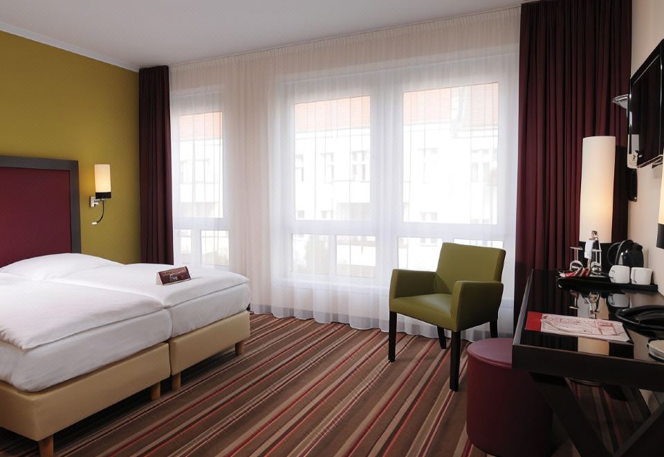 a hotel room with two beds , a window , and a chair , all situated in a modern and minimalist style at Leonardo Hotel Berlin