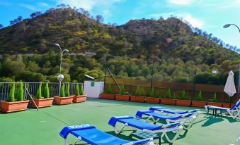 a green roof with blue chairs and umbrellas , surrounded by trees and a mountainous landscape at Hotel Maya Alicante