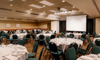 a large conference room with round tables and chairs , a projector screen , and multiple people in the background at Forest Park Hotel