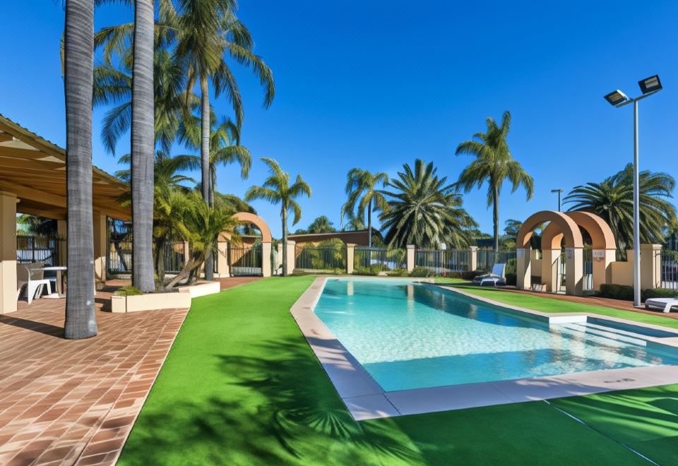 a large swimming pool is surrounded by palm trees and a green artificial grass surface at Ingot Hotel Perth, Ascend Hotel Collection