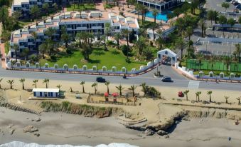 a beachfront resort with multiple buildings , palm trees , and a road is shown from an aerial view at Parador de Mojacar