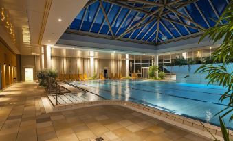 an indoor swimming pool with a glass ceiling , surrounded by lounge chairs and umbrellas , under the lights of night at Ibis Styles Chaumont Centre Gare