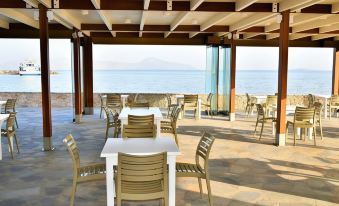 an outdoor dining area overlooking the ocean , with several tables and chairs arranged for guests to enjoy a meal at Mastichari Bay Hotel