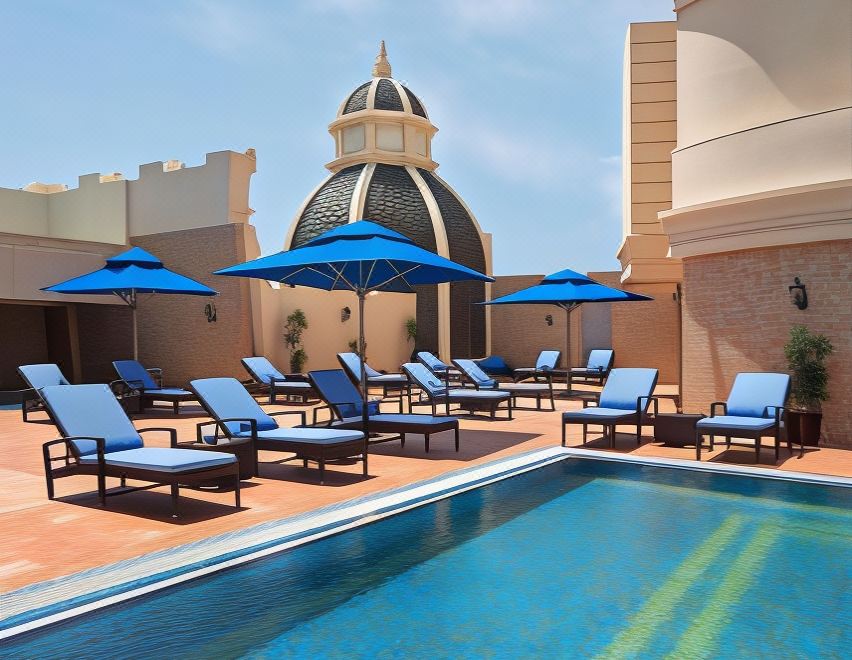 a rooftop pool with blue umbrellas , chairs , and tables surrounding the pool , providing a relaxing atmosphere for guests at Royal Rose Abu Dhabi