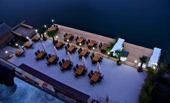 an aerial view of a large outdoor dining area with tables , chairs , and umbrellas by a body of water at Seehotel Gruner Baum