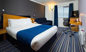 a modern hotel room with a blue and white color scheme , featuring a bed , a desk , and a chair at Holiday Inn Express Stafford