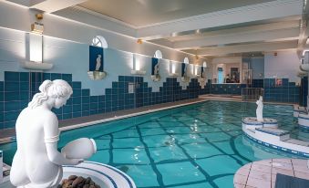 an indoor swimming pool with blue tiled walls and a white statue of a woman in the water at Castle Hotel Macroom