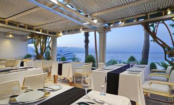 a restaurant with white tables and chairs , black tablecloths , and a view of the ocean at Steigenberger Hotel & Nelson Village, Taba