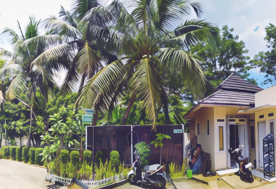 a person is sitting on a scooter in front of a building with palm trees at Bakom Inn Syariah