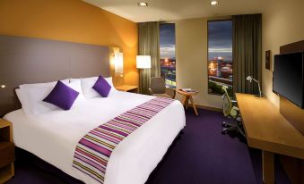 a large bed with white sheets and purple pillows is in a room with a desk , chair , and window at Hilton Garden Inn Monterrey Airport